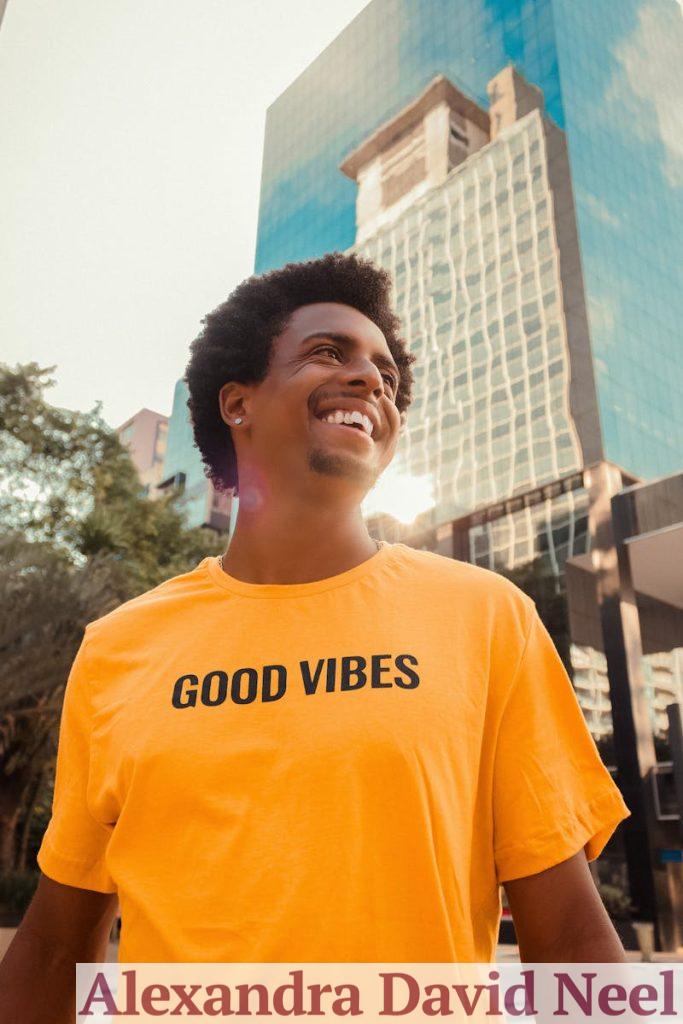 From below of cheerful African American male in bright yellow T shirt smiling and looking away near contemporary glass building